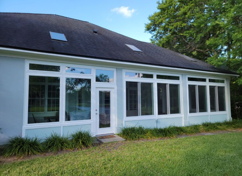 A light blue house with a sunroom, many windows and a door, and green grass.