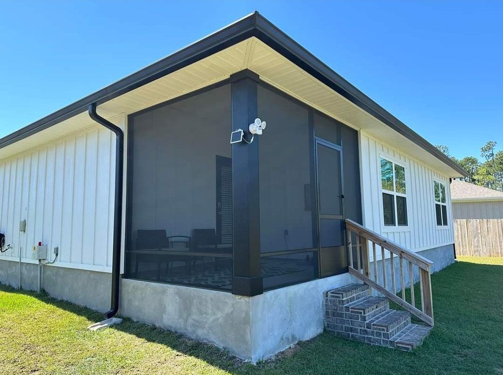 Screened-in porch attached to a white-sided house with black trim and a small set of brick stairs.