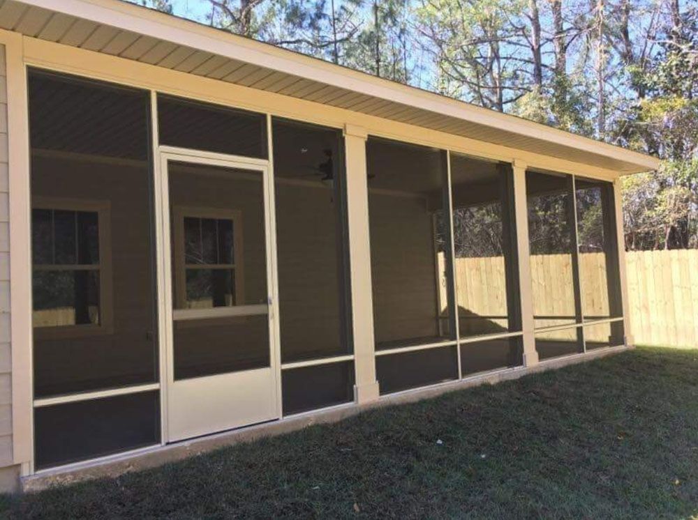Screened porch with white trim, door, and windows, overlooking a grassy yard with trees in the background.