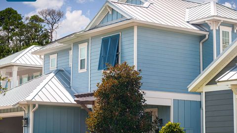 Blue house with white trim, metal roof, open shutter, and green tree in front.