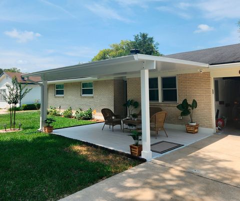 Covered patio attached to a brick house with chairs, plants, and a rug.