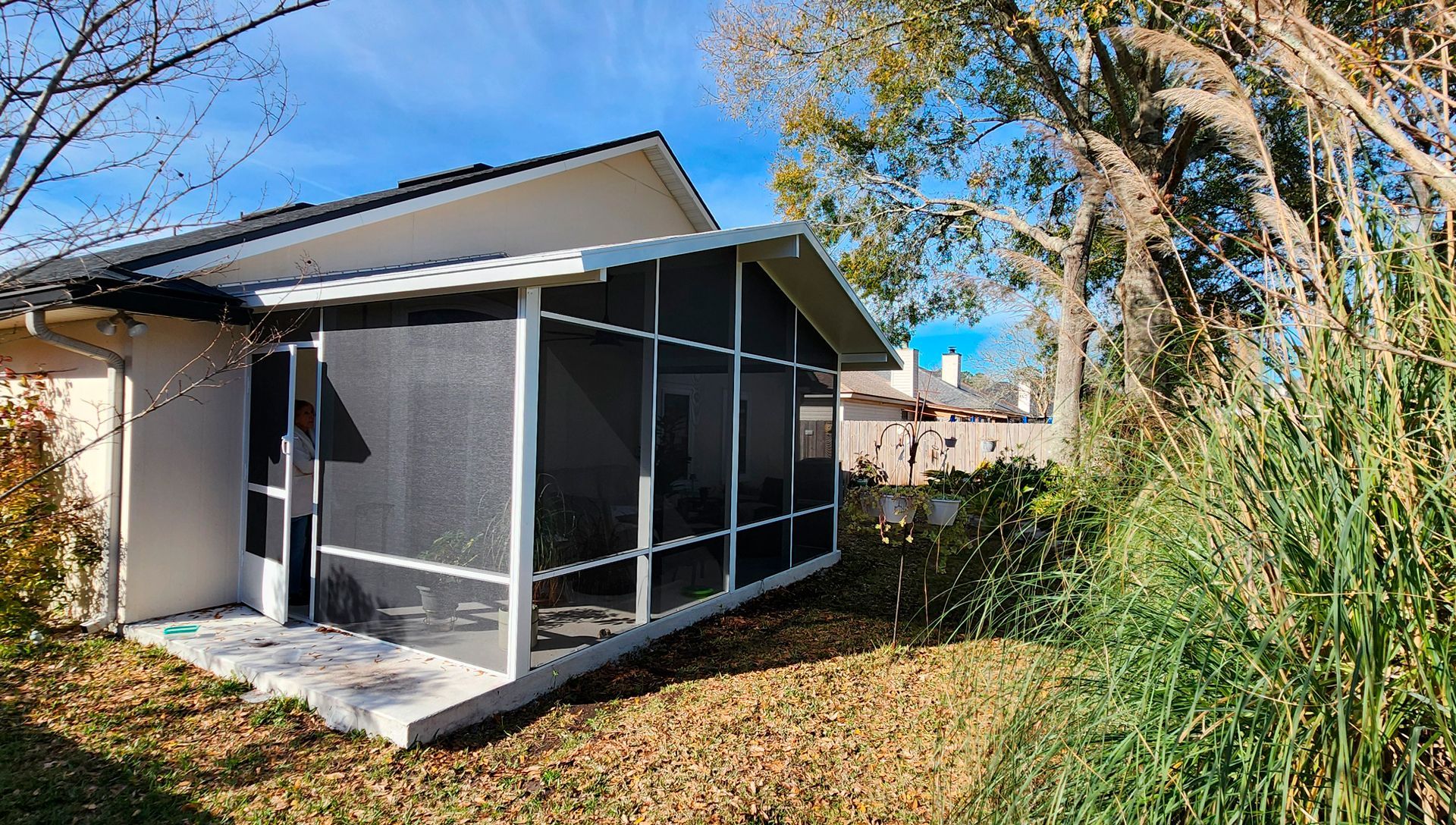 Screened-in patio attached to a house with tall grass and trees in the background.
