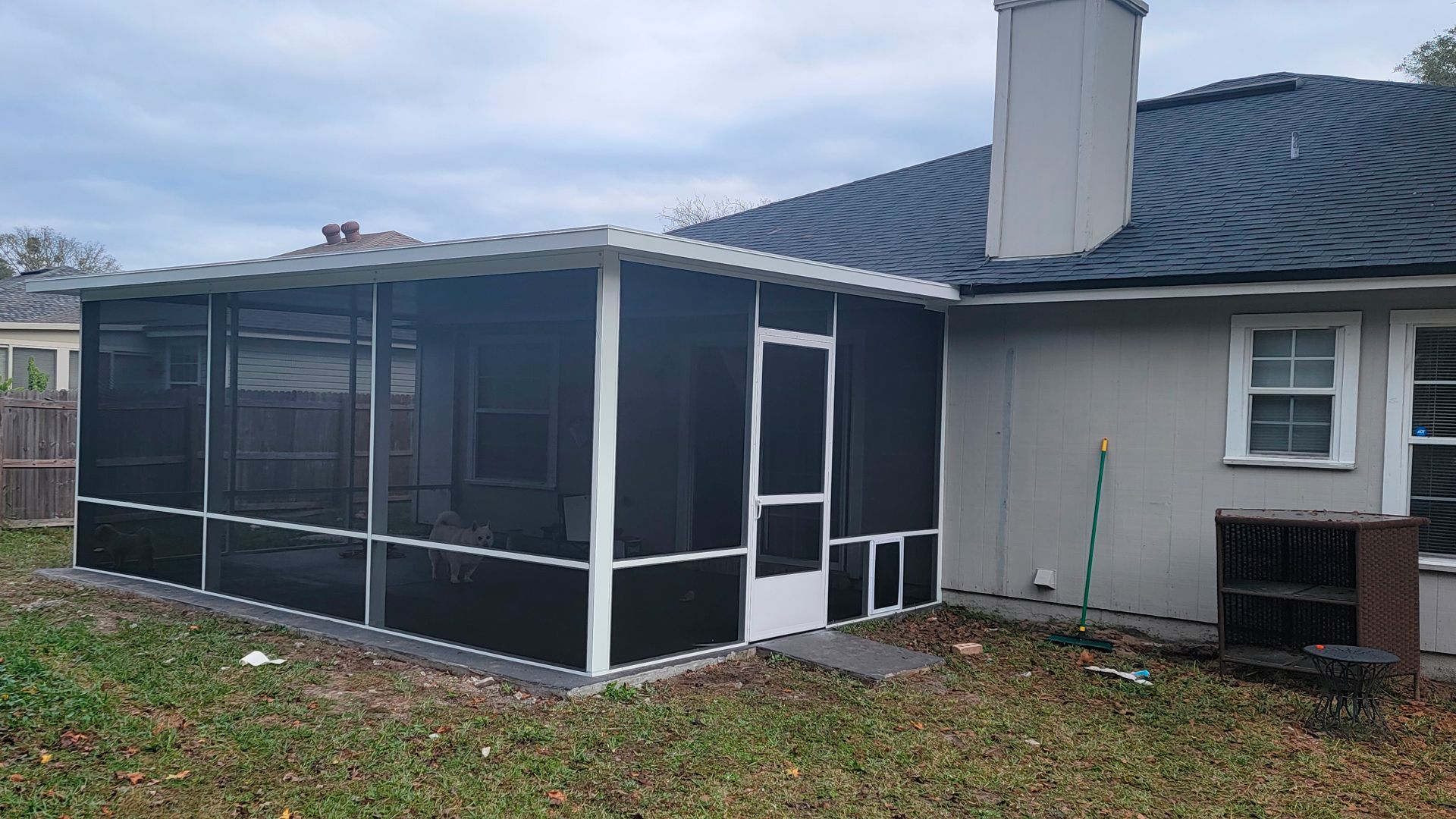 Screened-in porch attached to a house with black screens, white trim, and a door. Overcast sky.