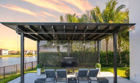 Outdoor pergola with TV, lounge chairs, and lake view. Black structure, green grass, and sunset sky.