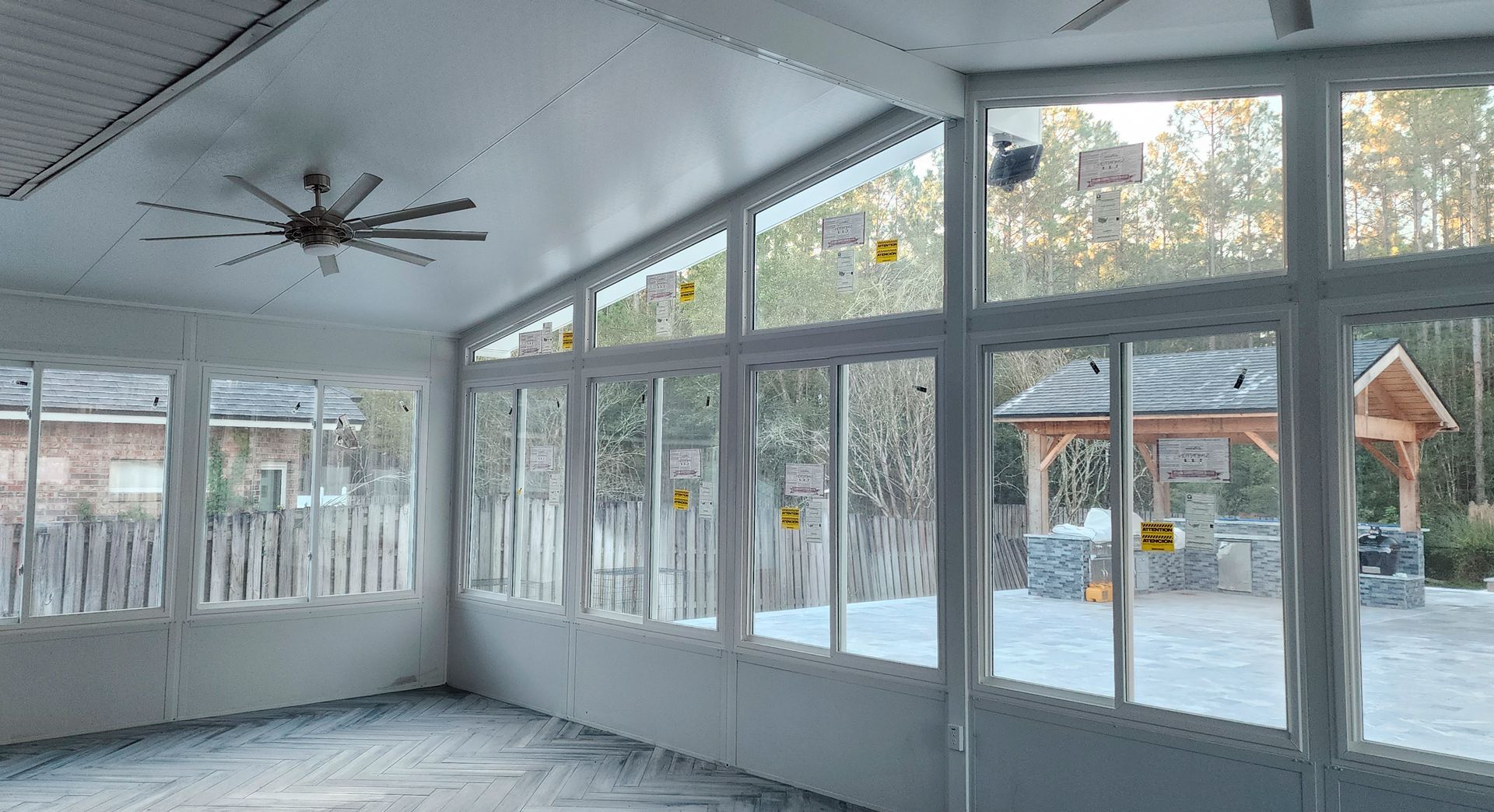Sunroom interior with large windows and a ceiling fan, overlooking a backyard.