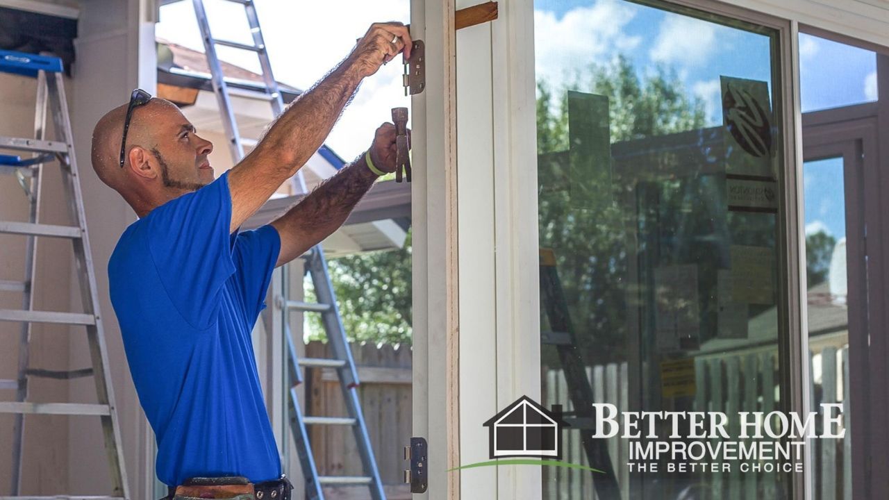 Man installing door, outdoors. White door frame, ladder, blue shirt, sunny day.