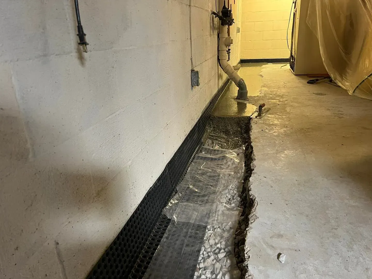 Basement corridor with exposed concrete floor, wall drain, and a water leak pooling along the edge