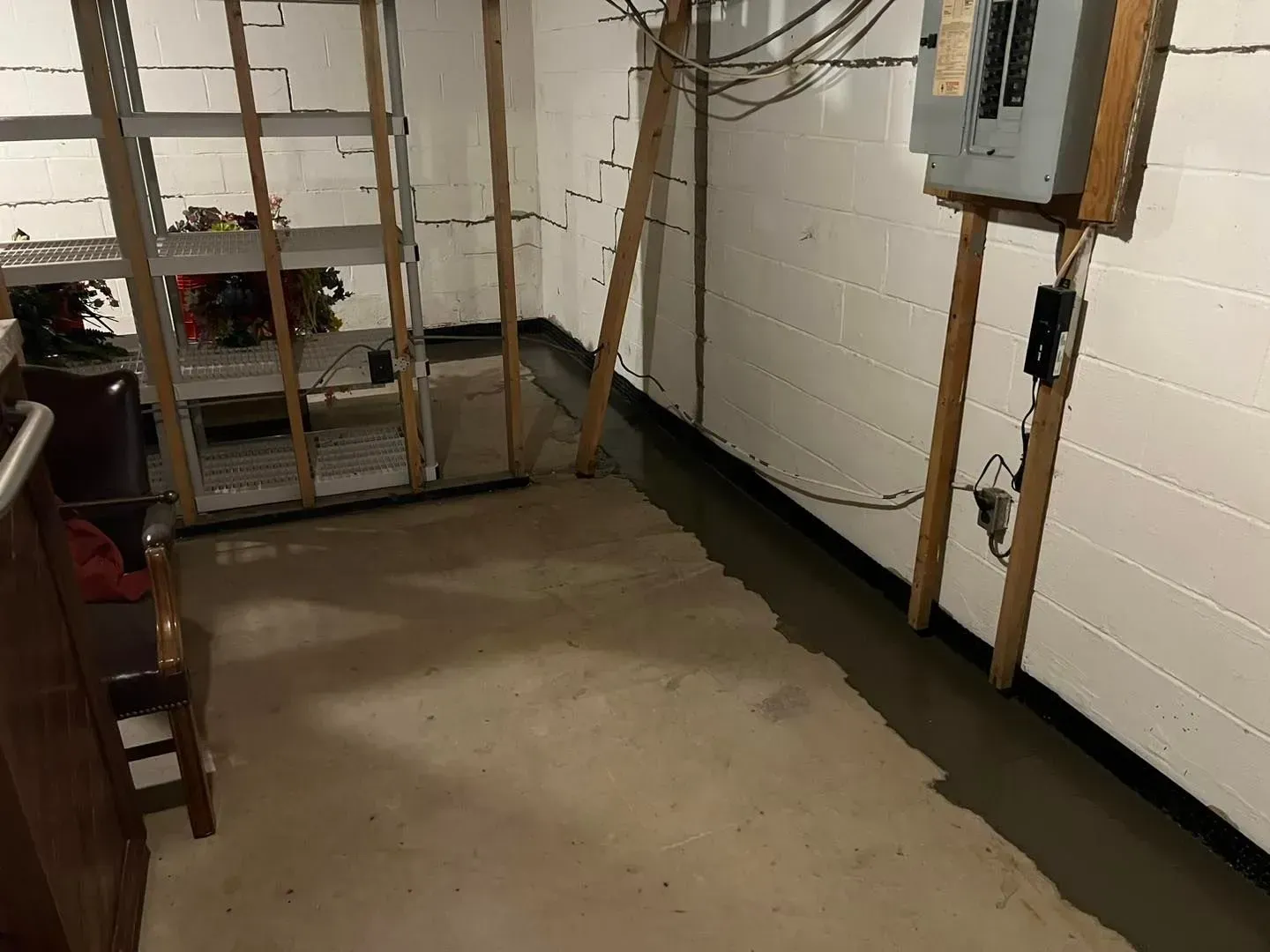 Basement utility room with concrete floor, white walls, exposed pipes, and shelving against the back wall