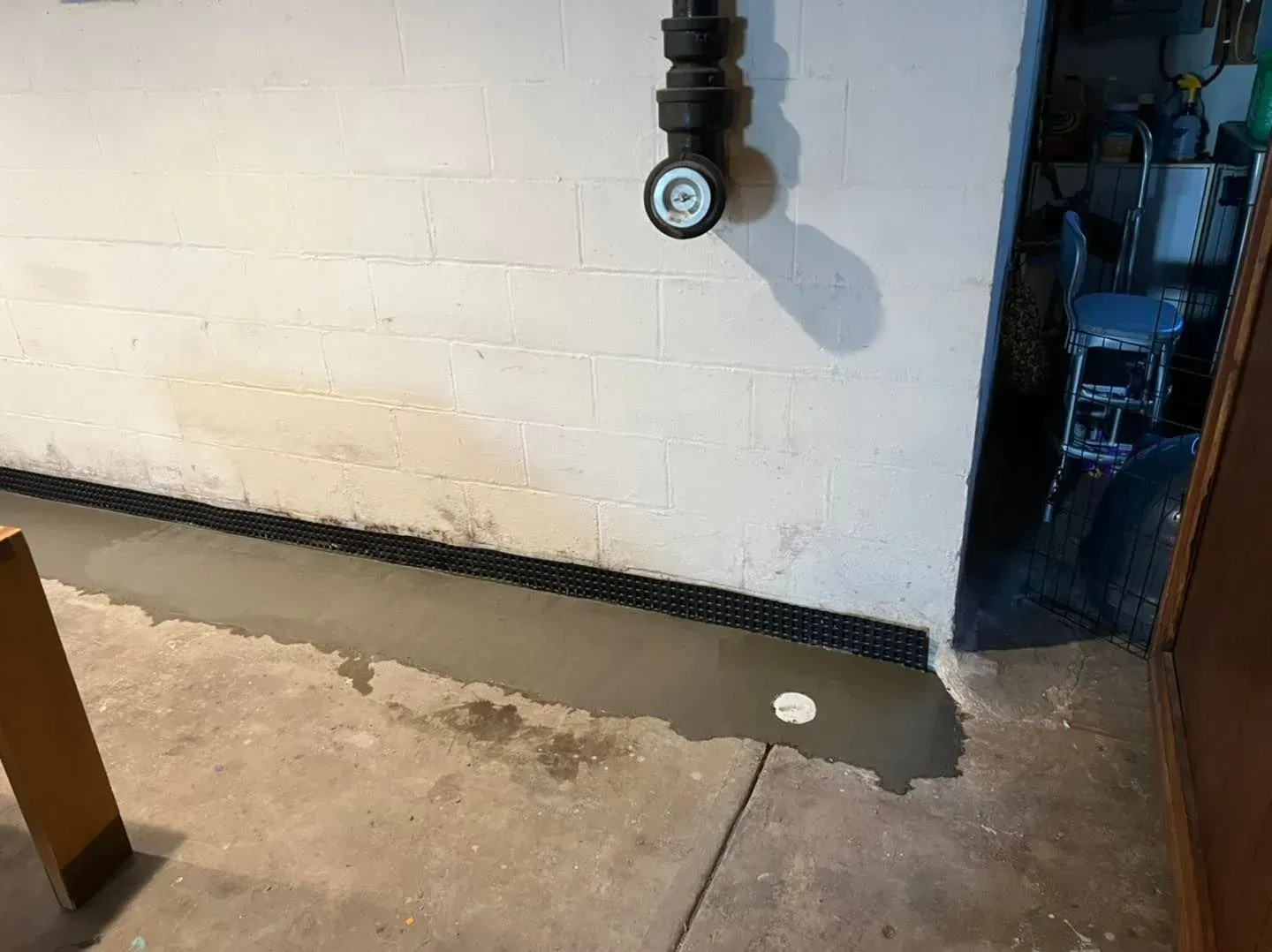 Basement wall with exposed pipe and wet concrete floor near a doorway