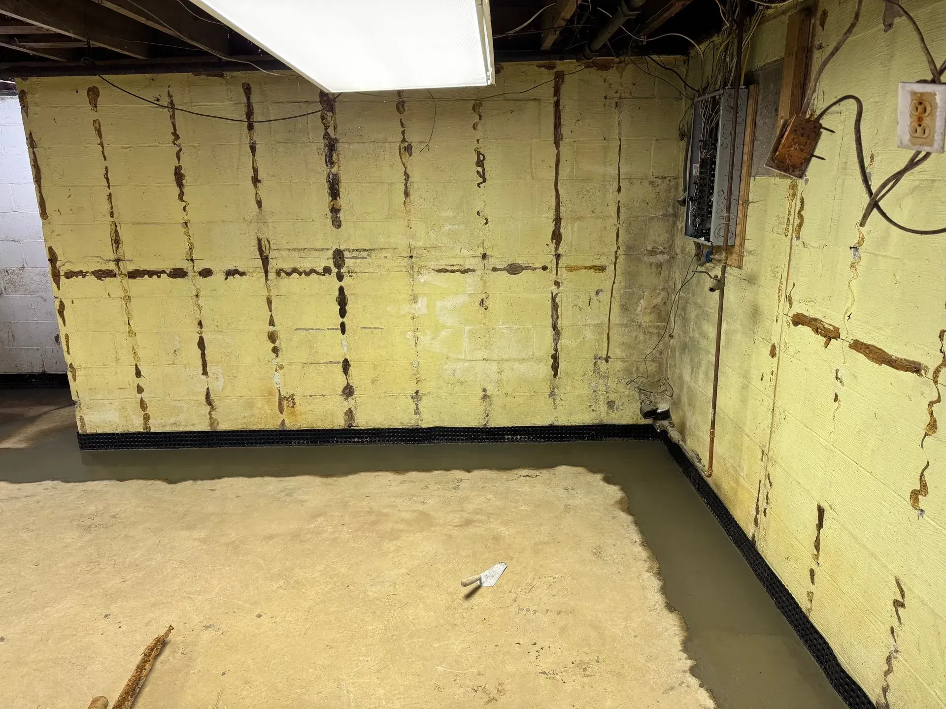 Empty unfinished basement with yellow insulated walls and concrete floor, showing water along the edges