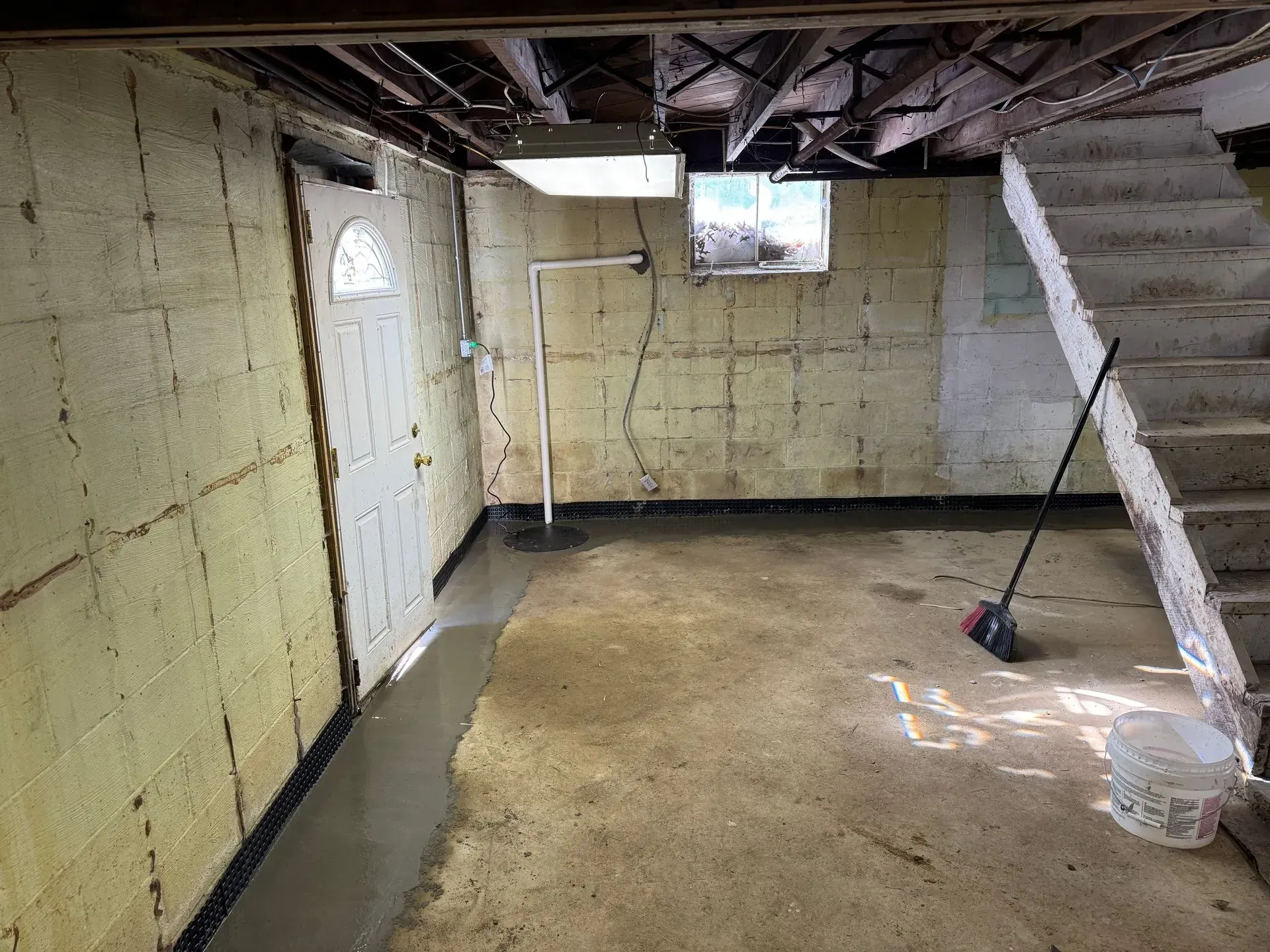 Unfinished basement with insulated walls, exposed ceiling beams, concrete floor, and staircase on the right.