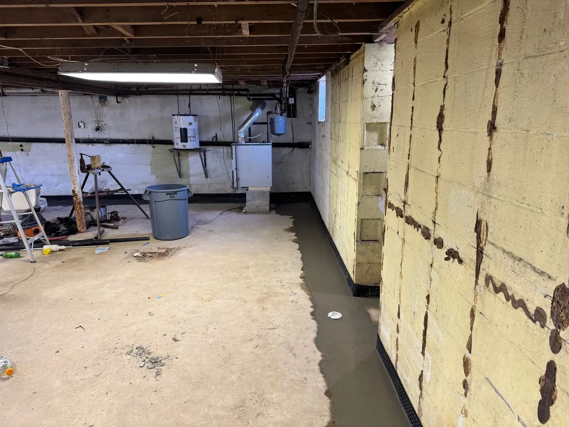 Unfinished basement with exposed ceiling beams, insulation walls, and tools scattered on a concrete floor.