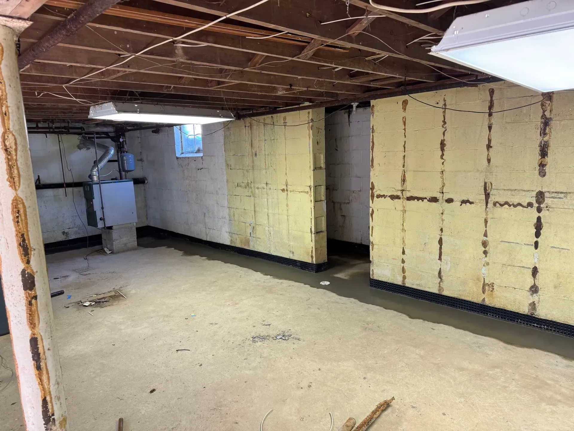 Unfinished basement with exposed ceiling joists, yellow insulation walls, concrete floor, and a small window.