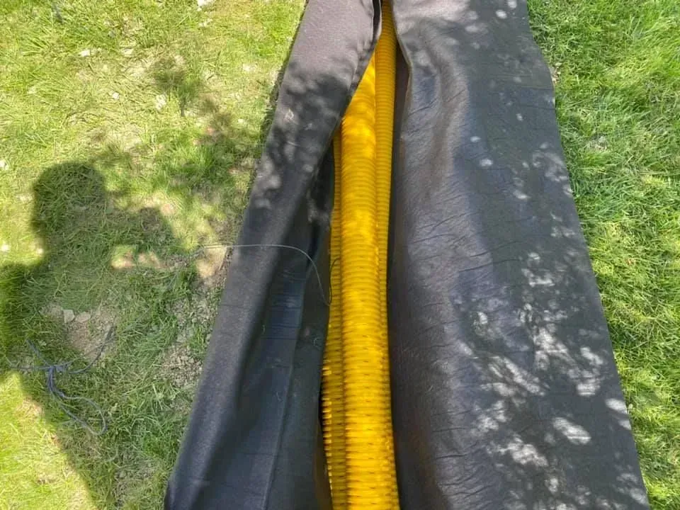 Black and yellow hose or cable lying on grass beside a paved path