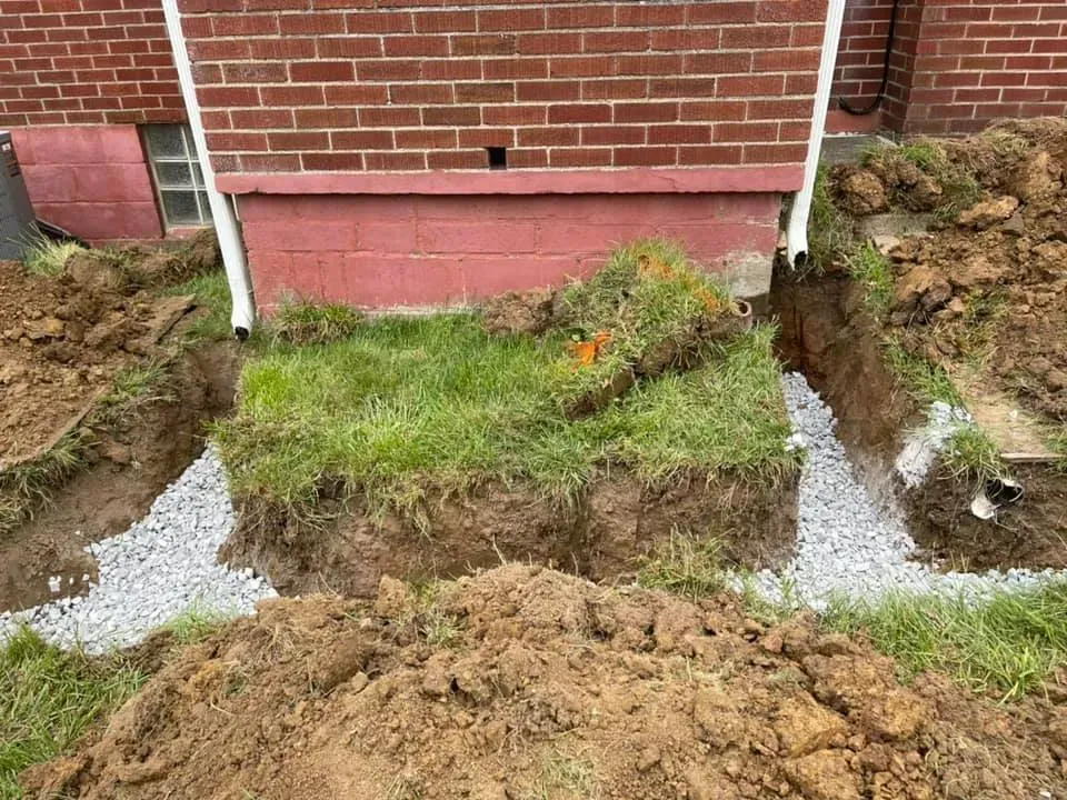 Garden bed under brick wall with fresh soil, green grass, and gravel paths on both sides