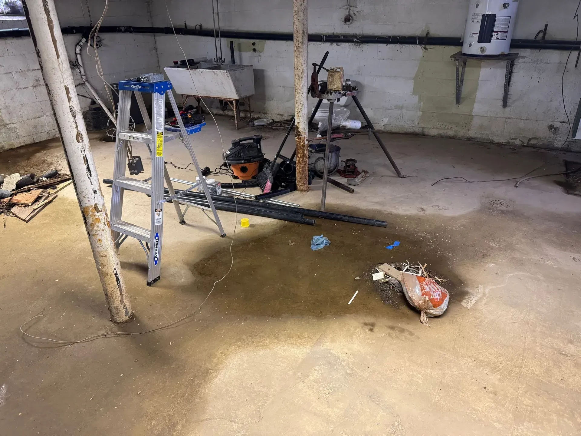 Flooded basement with a ladder, tools, and a saw on the floor amid muddy water.