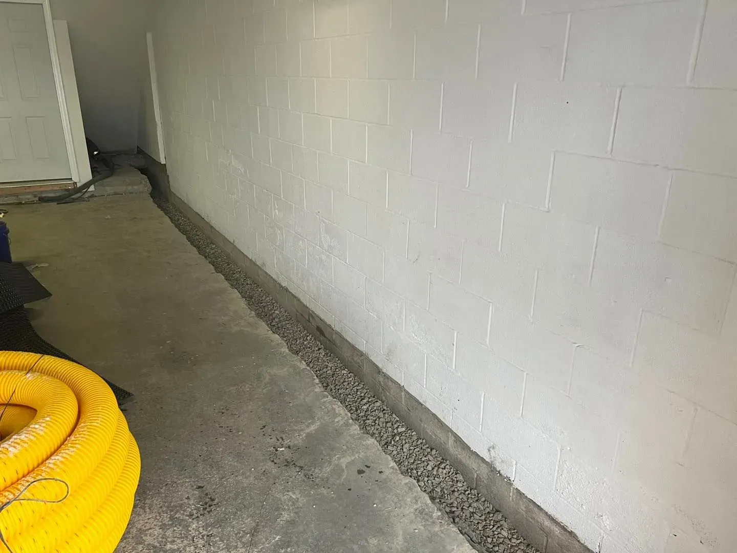 Narrow concrete corridor with white block walls and a coiled yellow hose in the foreground.