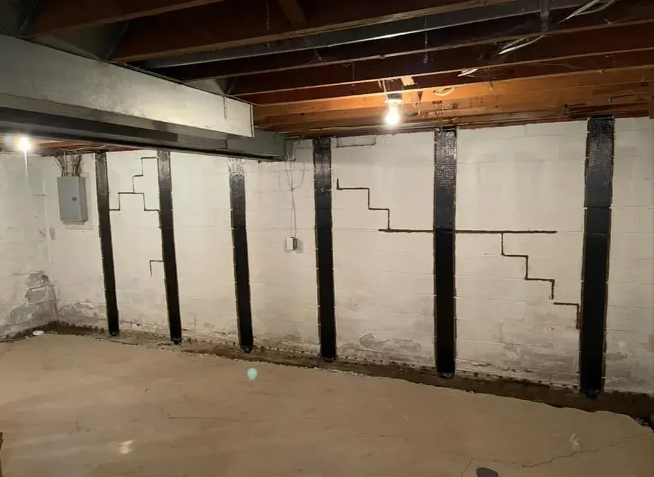 Basement wall with black support beams, exposed ceiling joists, and rough white brick walls.
