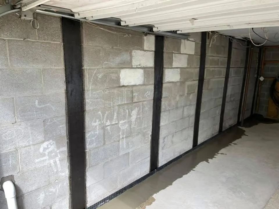 Concrete block basement wall with vertical black support beams and a concrete floor