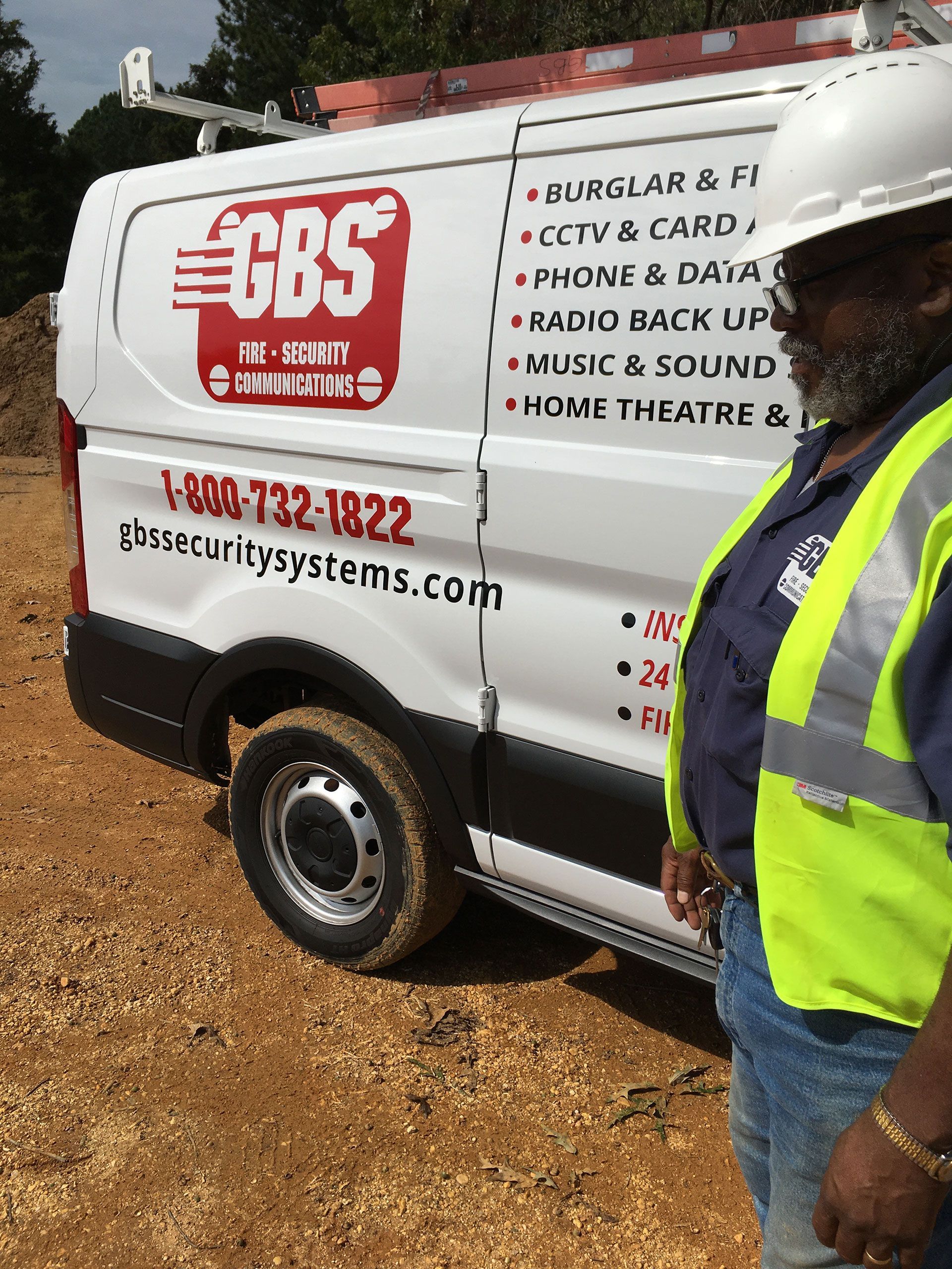 A man in a yellow vest is standing in front of a cbs van