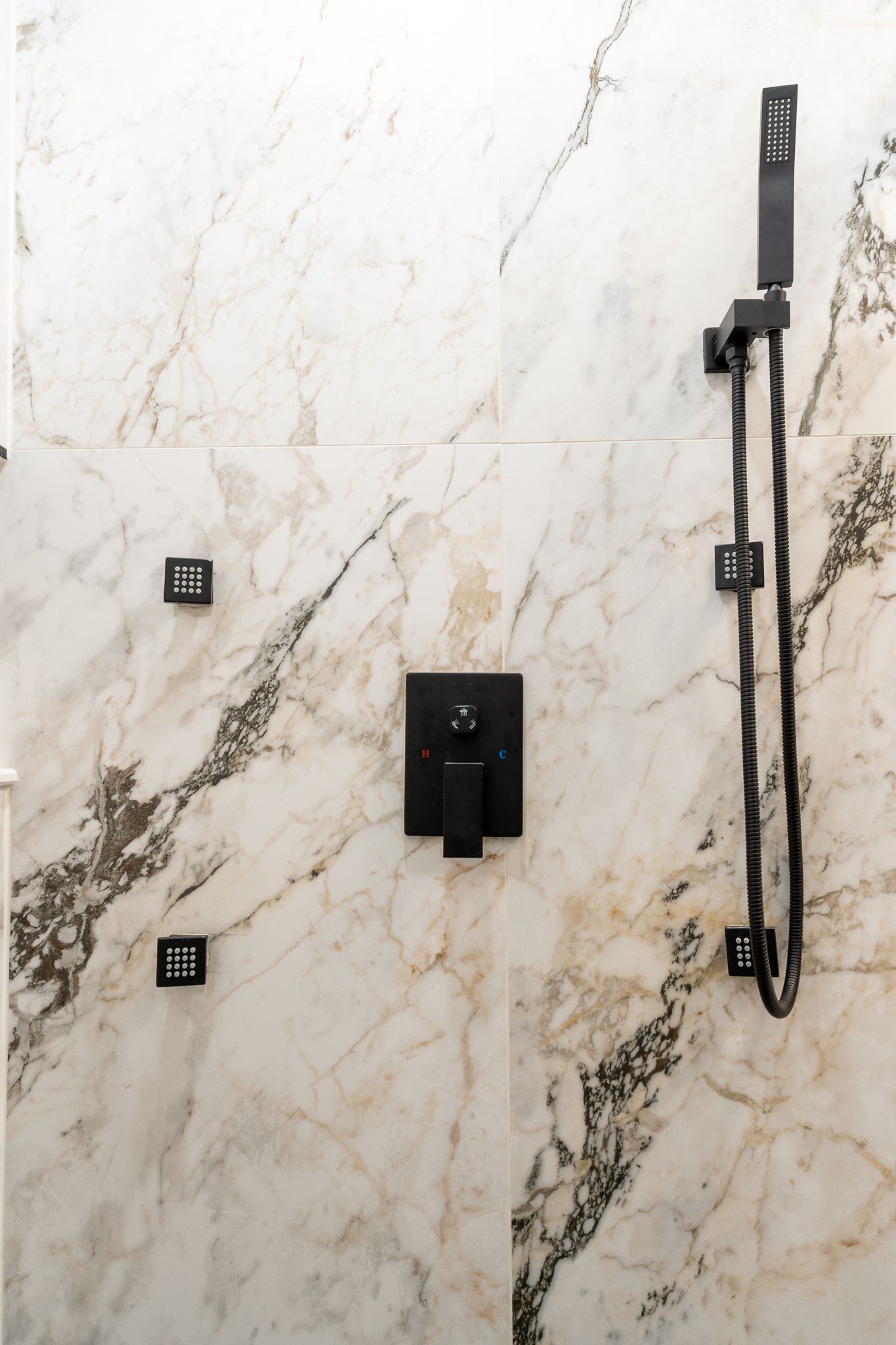 A shower with a black shower head on a marble wall.