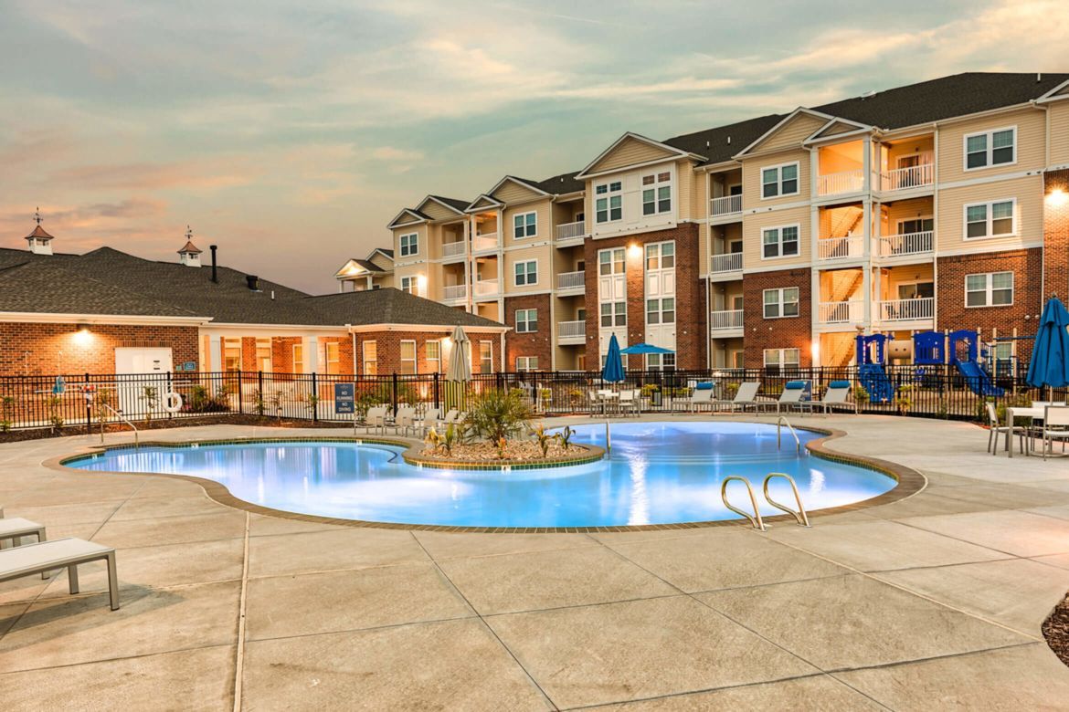 Apartment complex pool with blue water, lounge chairs, and building in the background.