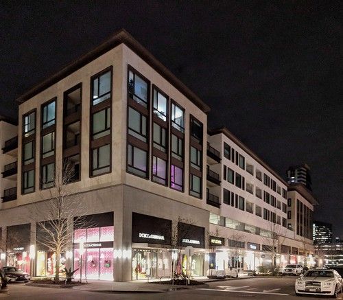 Night view of a modern building with lit shop windows and apartments above, along a street.