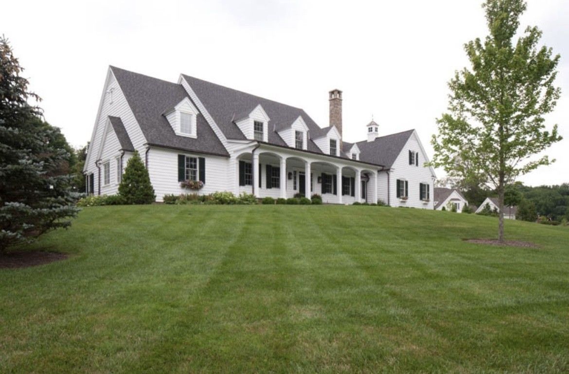 White house on a grassy hill, with black shutters and a dark roof.