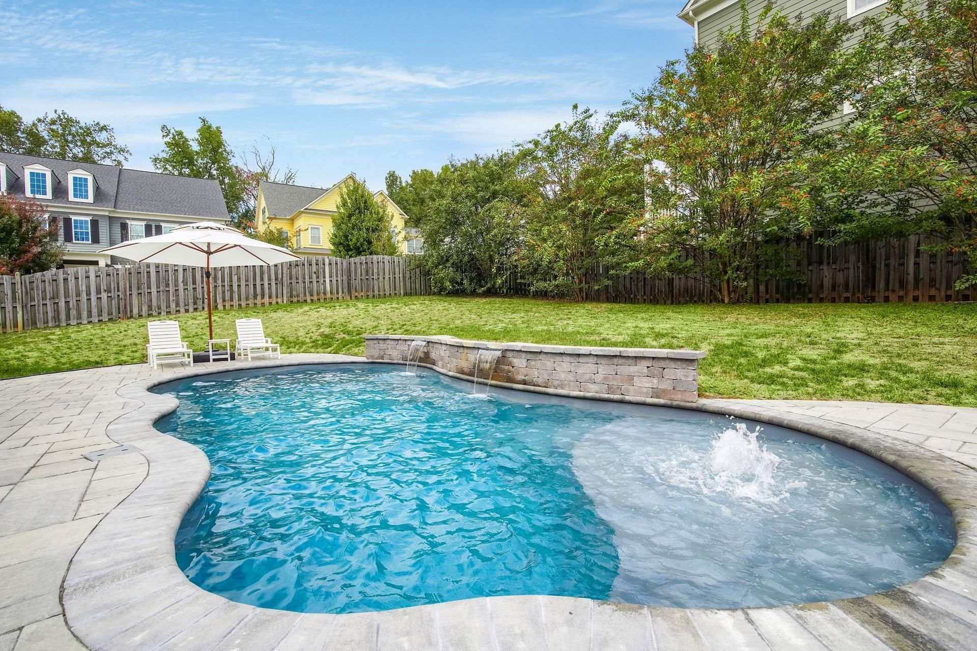 Backyard with a blue, freeform pool, patio, green lawn, and neighboring houses.