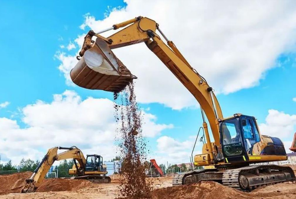 Yellow excavator dumping soil at a construction site.