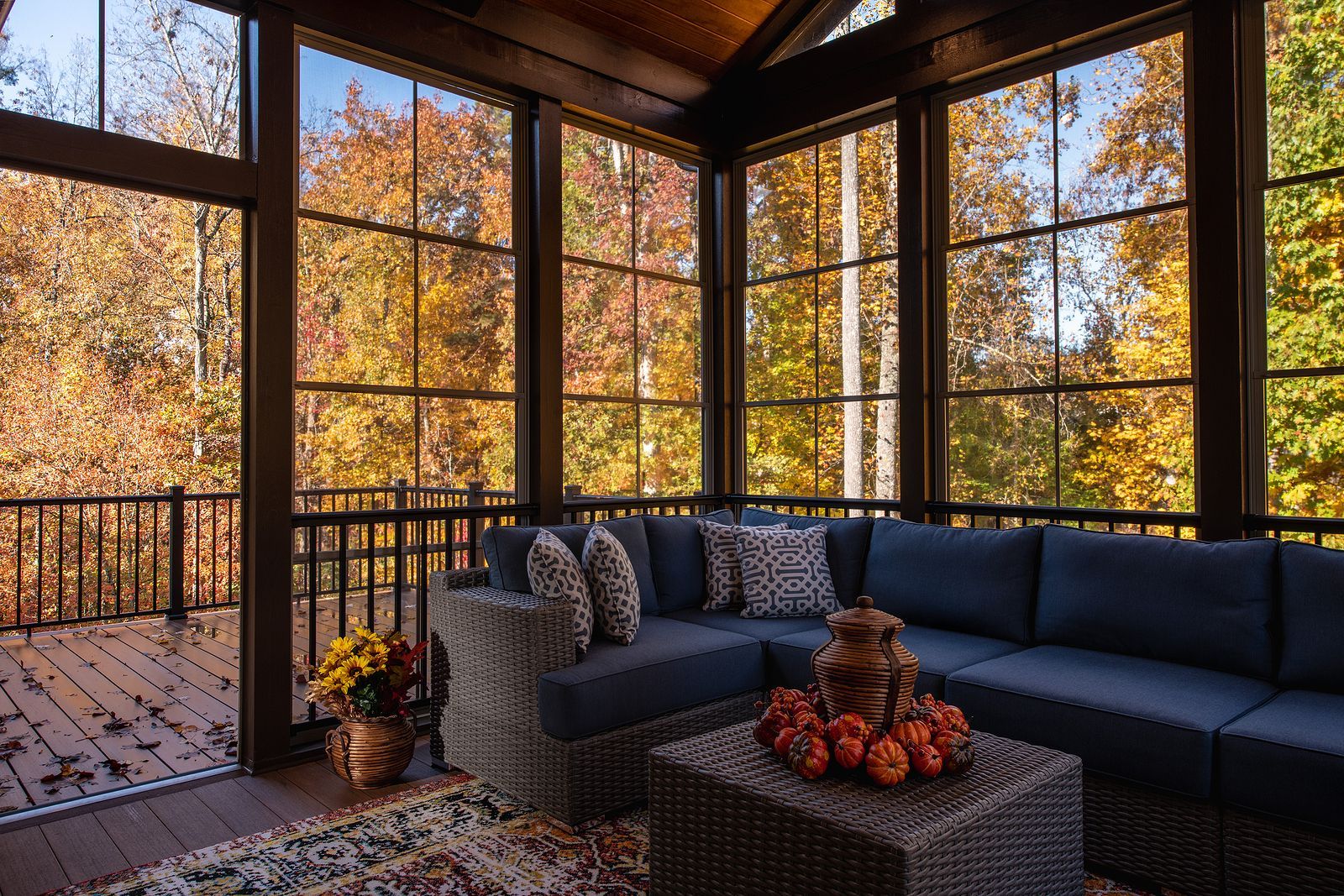 A screened porch with a dark blue sectional sofa and a coffee table overlooking fall foliage.