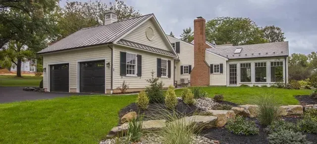 A large white house with a garage and a chimney is sitting on top of a lush green hillside