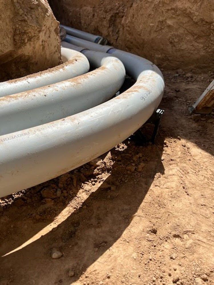 Gray electrical conduit pipes snaking through a dirt trench.