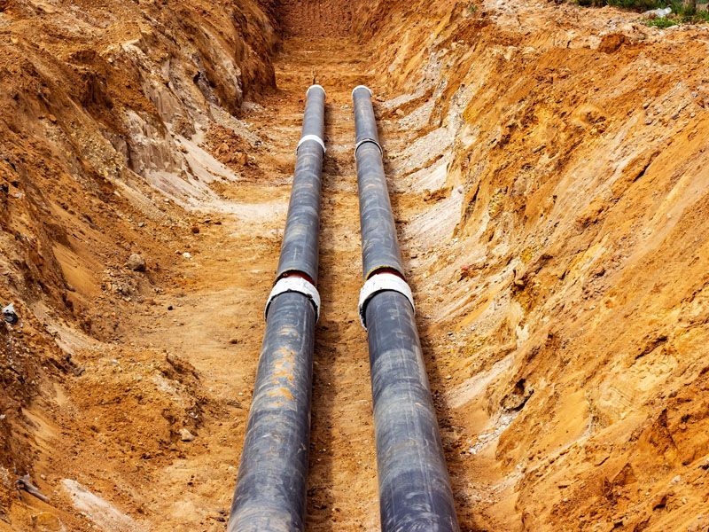Two black pipes lie in a trench of brown earth.