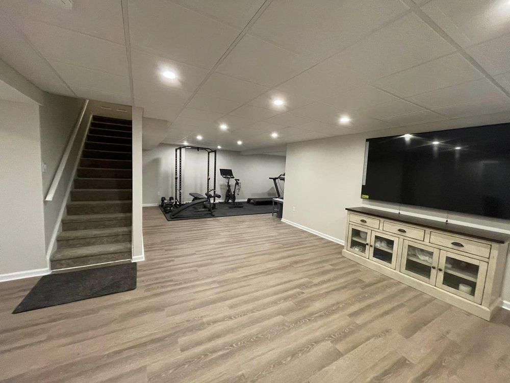 A basement with hardwood floors, stairs, a treadmill and a flat screen tv