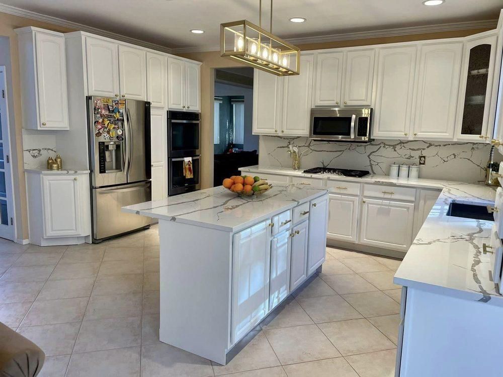 A kitchen with white cabinets, marble counter tops, stainless steel appliances and a large island