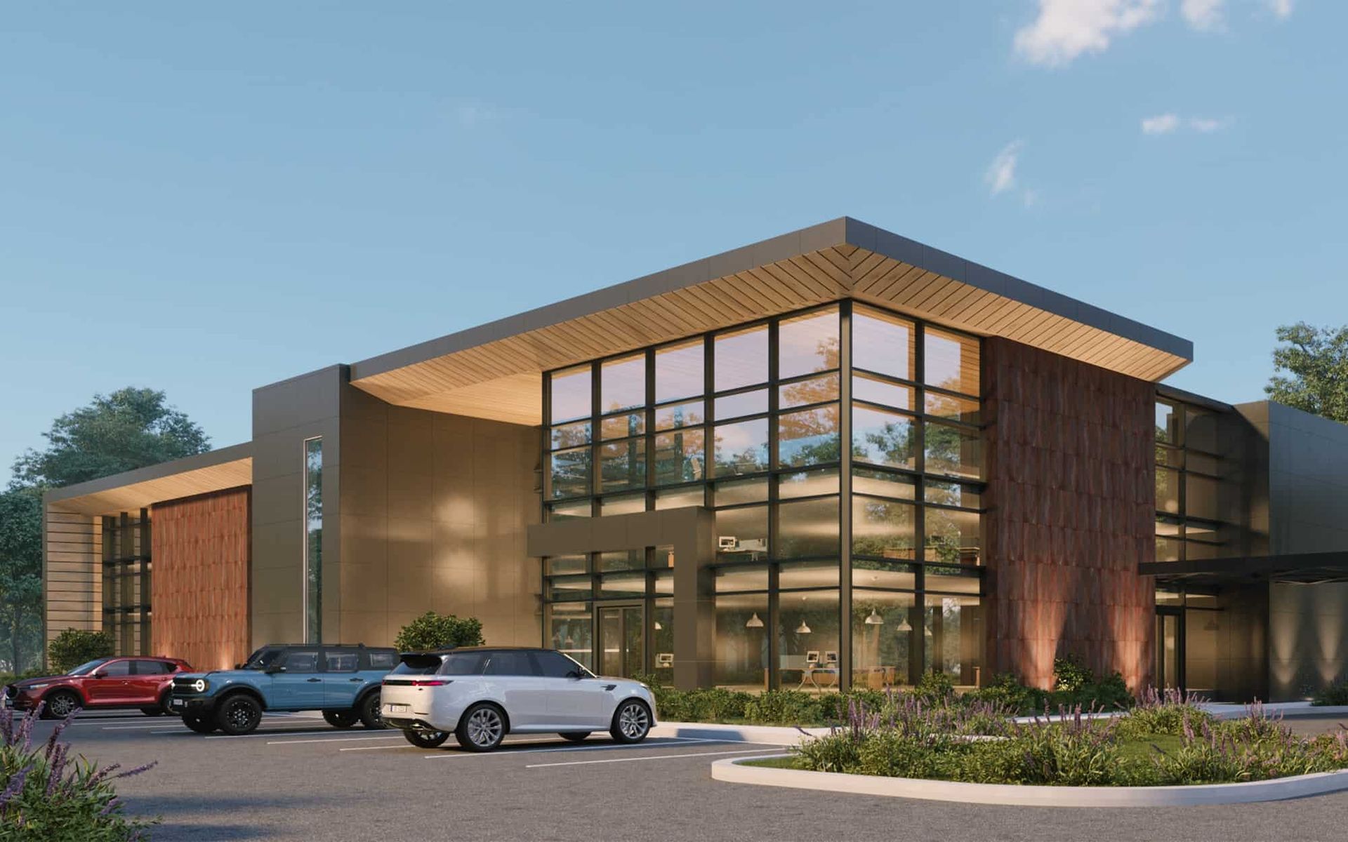 Modern building exterior with glass windows, cars parked out front, and landscaping.