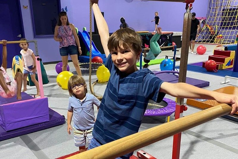 A young boy is standing on a balance beam in a gym.