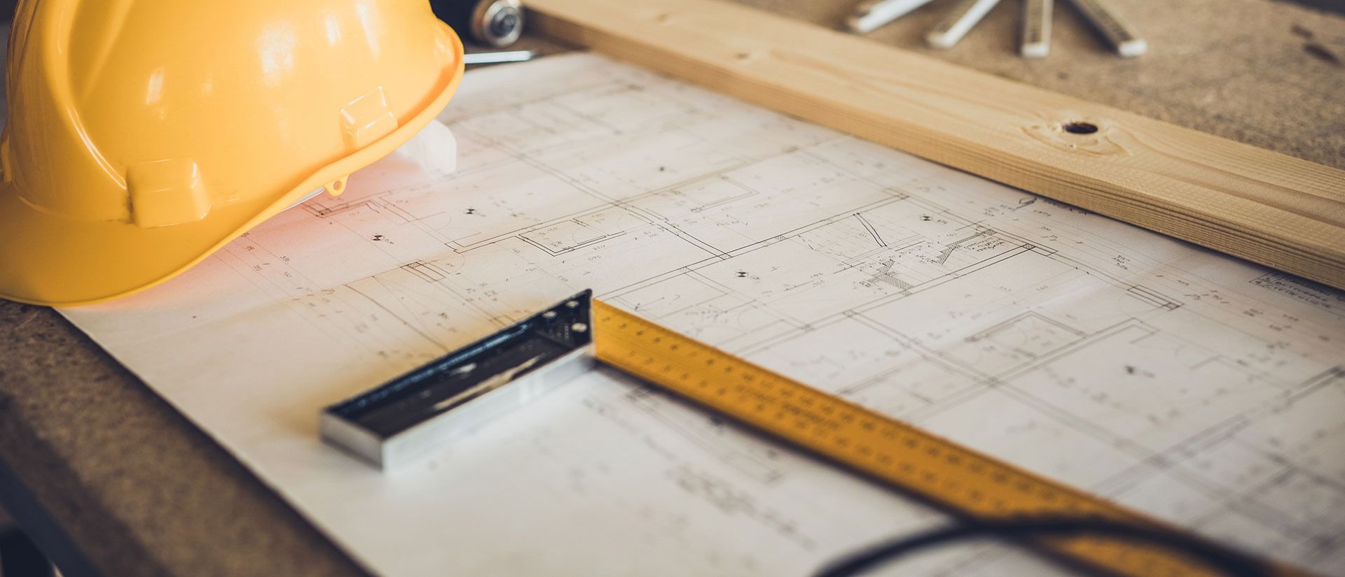 Yellow hard hat, ruler, and blueprint on a wooden surface, construction concept.