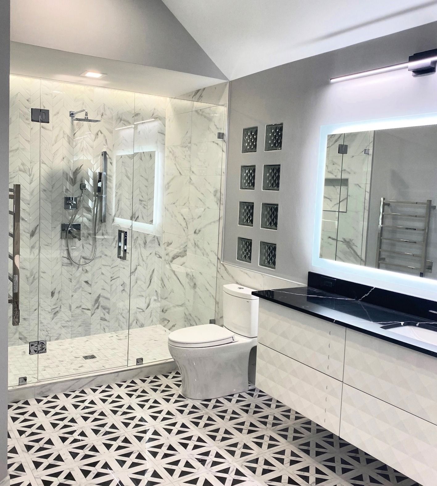 Modern bathroom with marble shower, patterned floor, white vanity, and glass block accent.