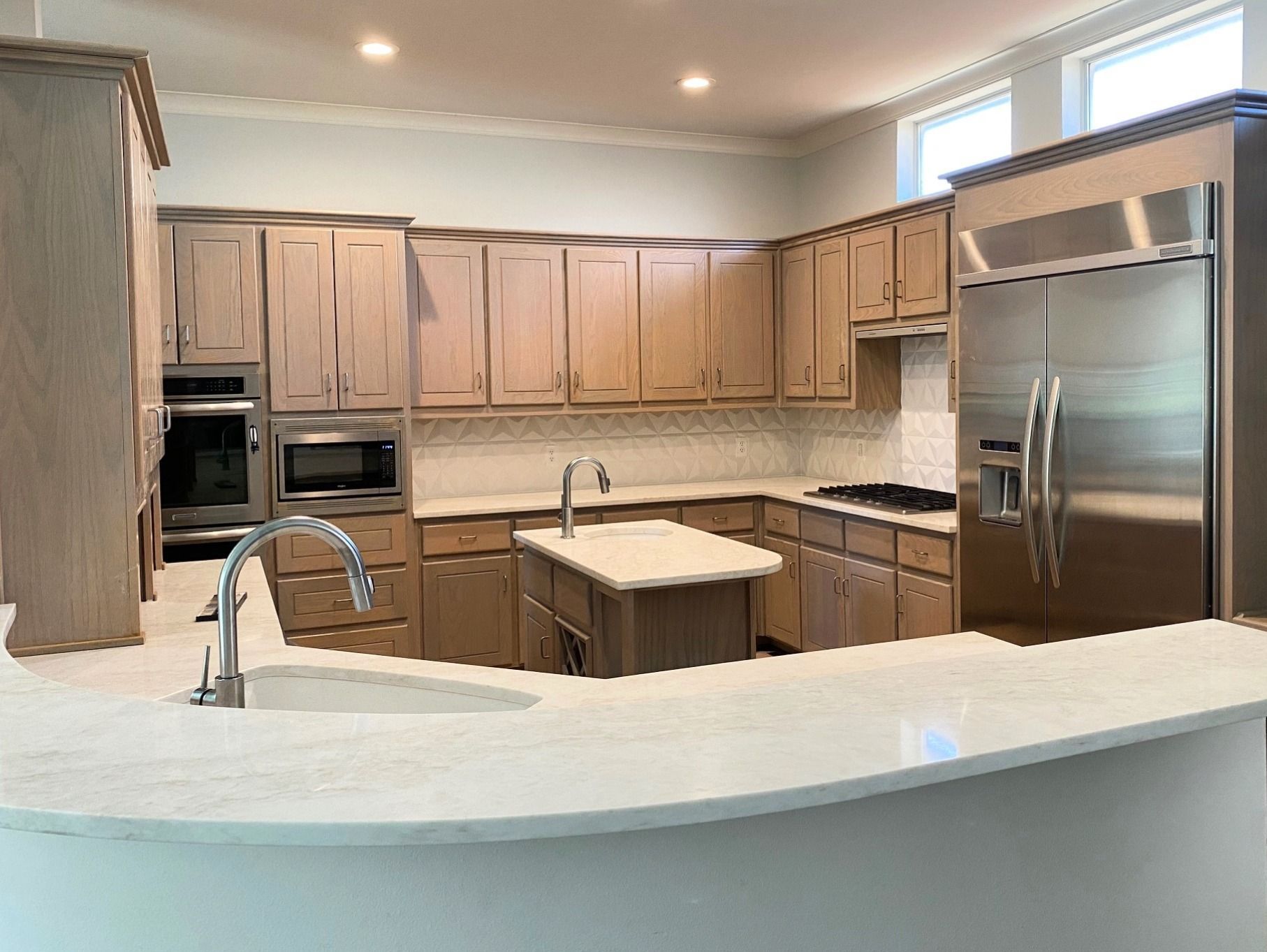 A modern kitchen with light brown cabinets, stainless steel appliances, and a white countertop.