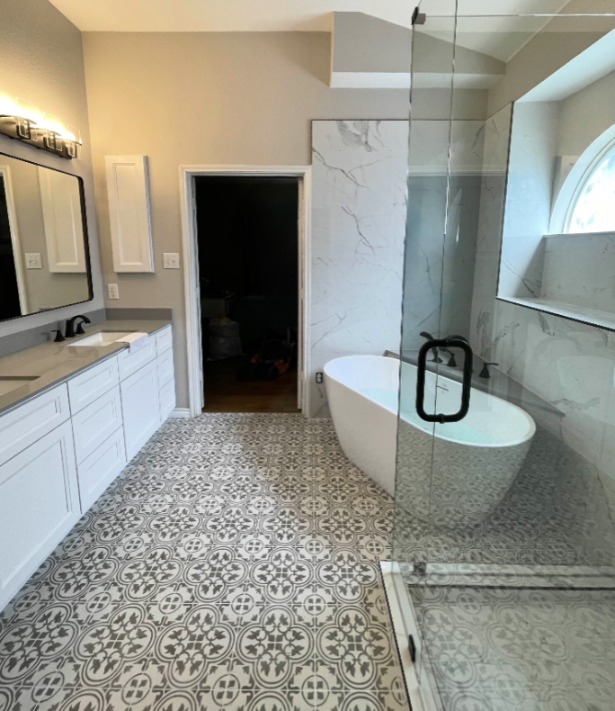 Bathroom with patterned floor, white cabinets, freestanding tub, glass shower, and marble accent wall.