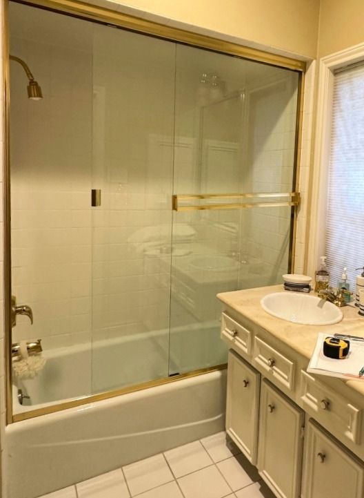 Bathroom with white tub, gold-framed glass shower doors, vanity, and sink; gold fixtures.