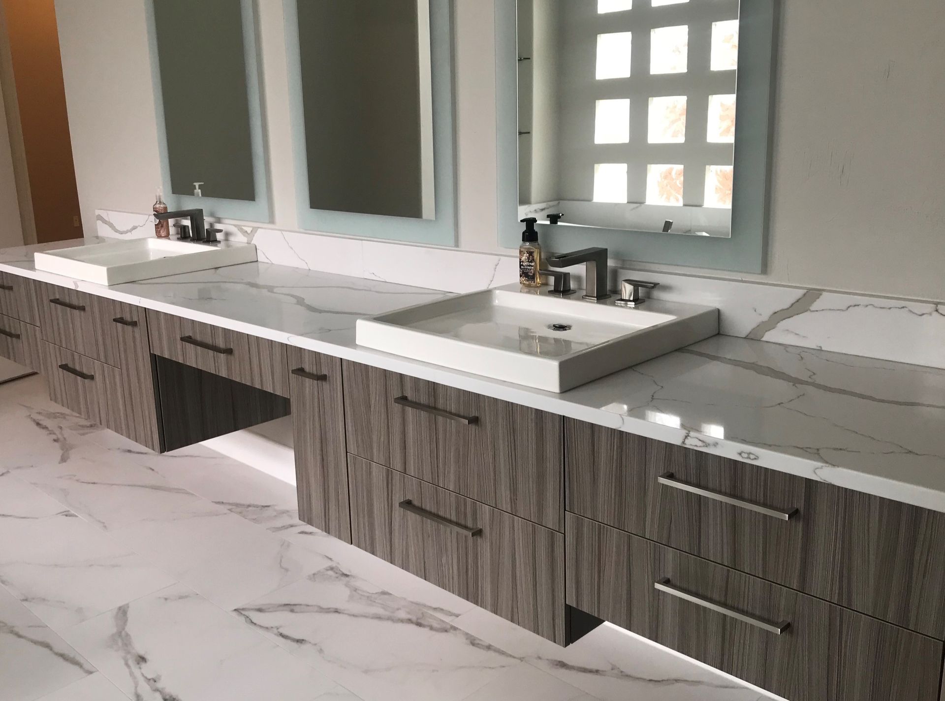 Modern bathroom with two sinks, marble countertops, and light-wood cabinets.