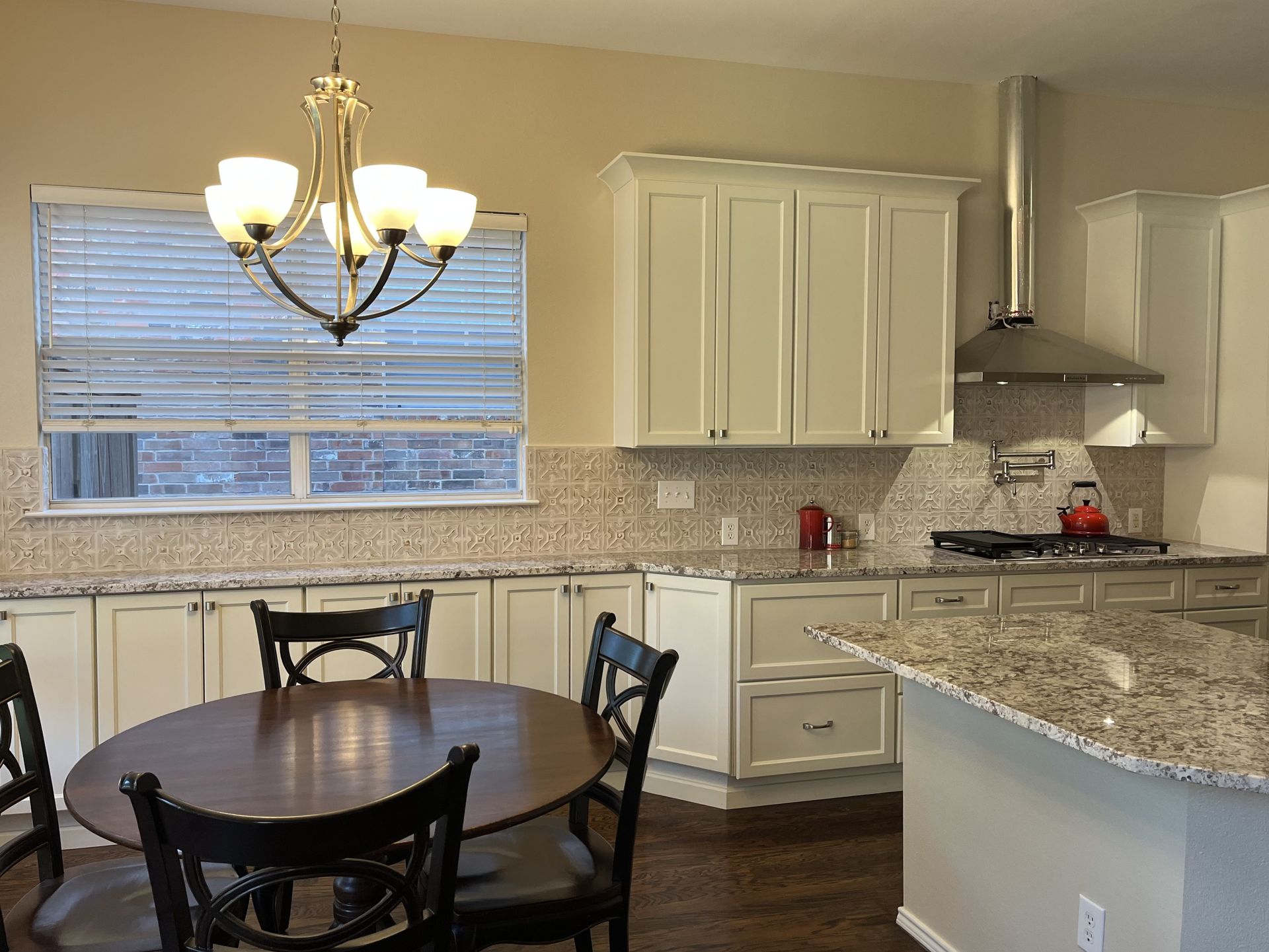 Kitchen with white cabinets, dark table, chandelier, and a stove with a vent hood.