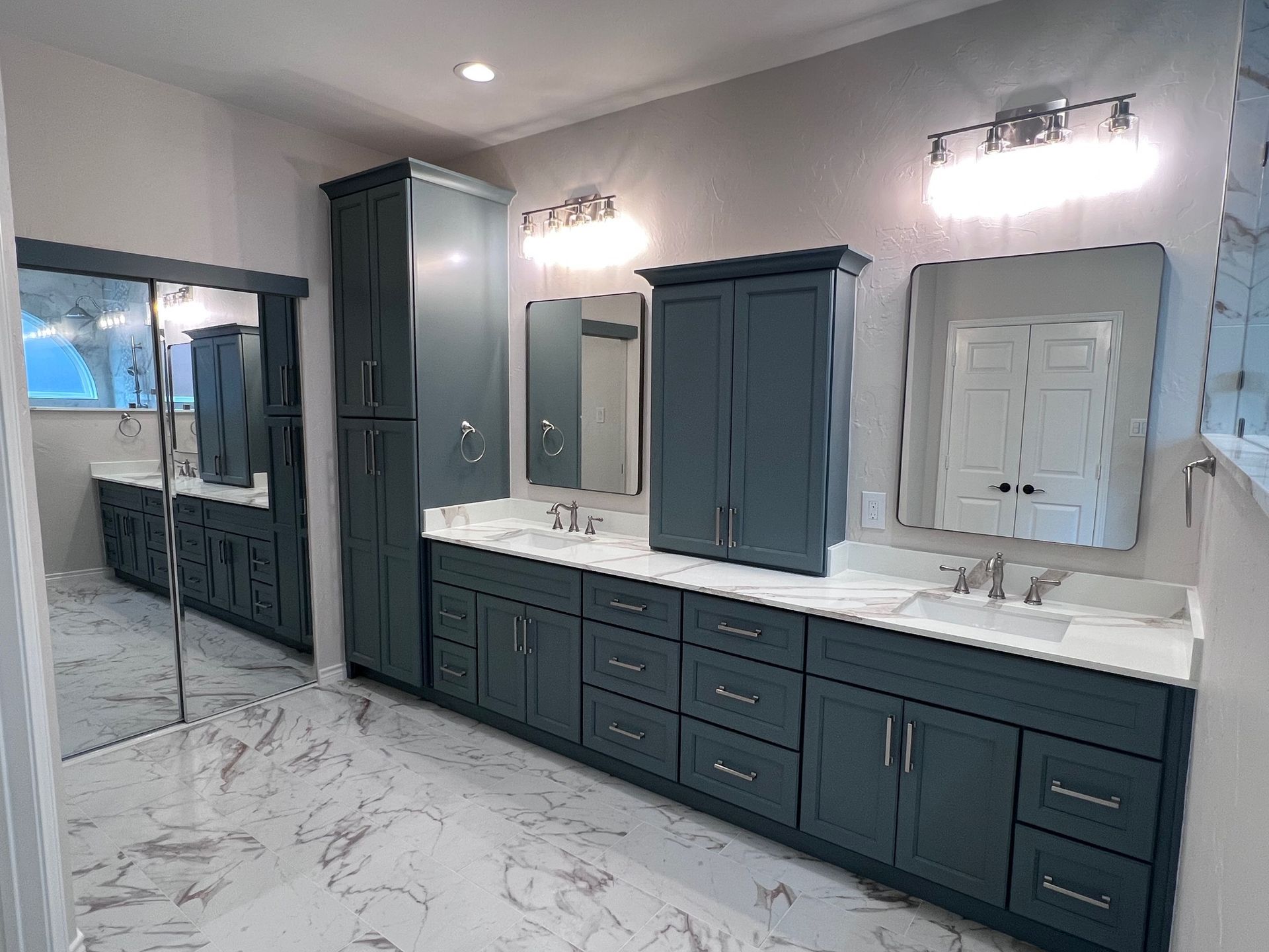 Bathroom with blue cabinets, white countertops, marble floors, and mirrors.
