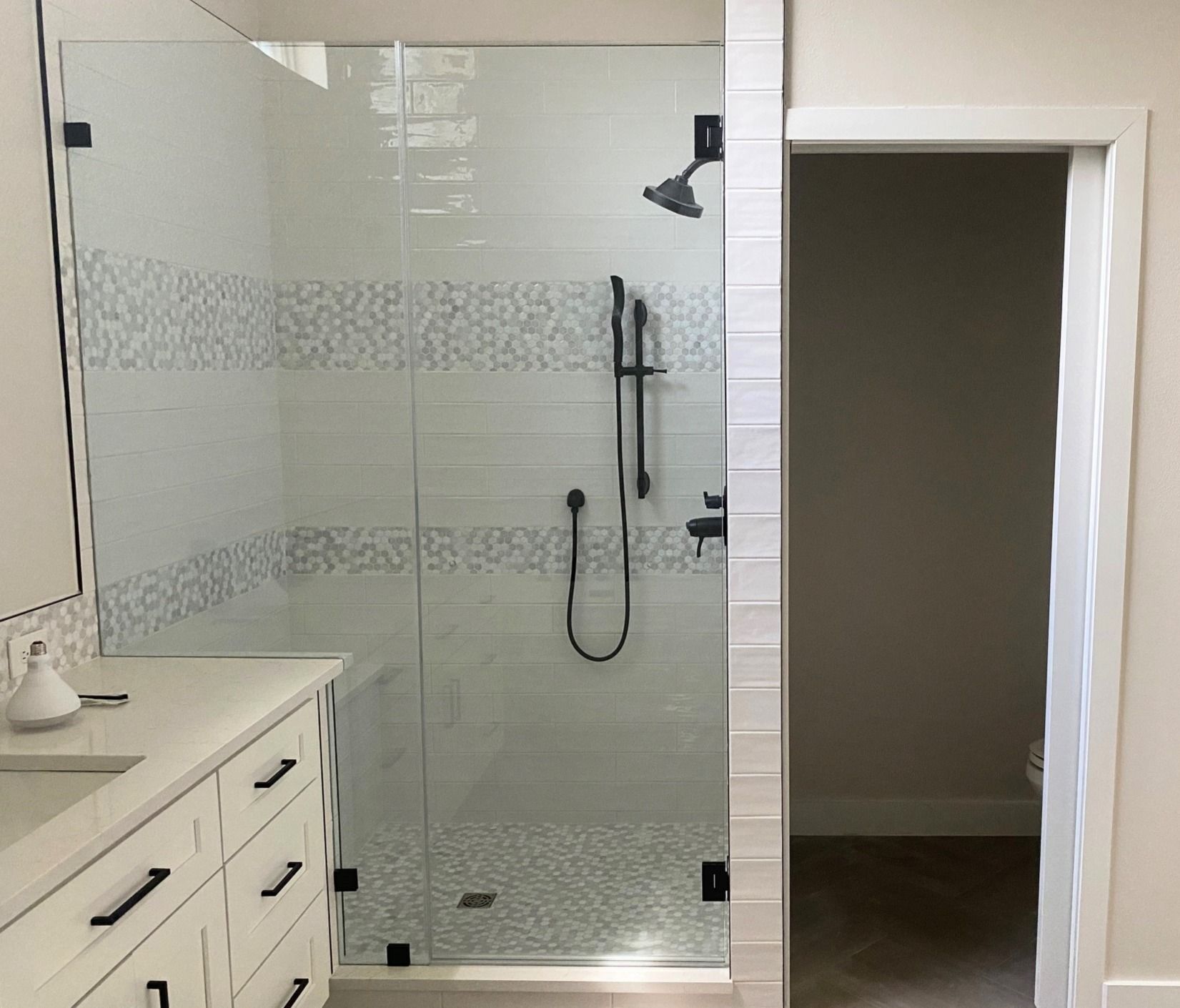 Modern bathroom with glass shower, white vanity, black fixtures, and neutral tiled walls.