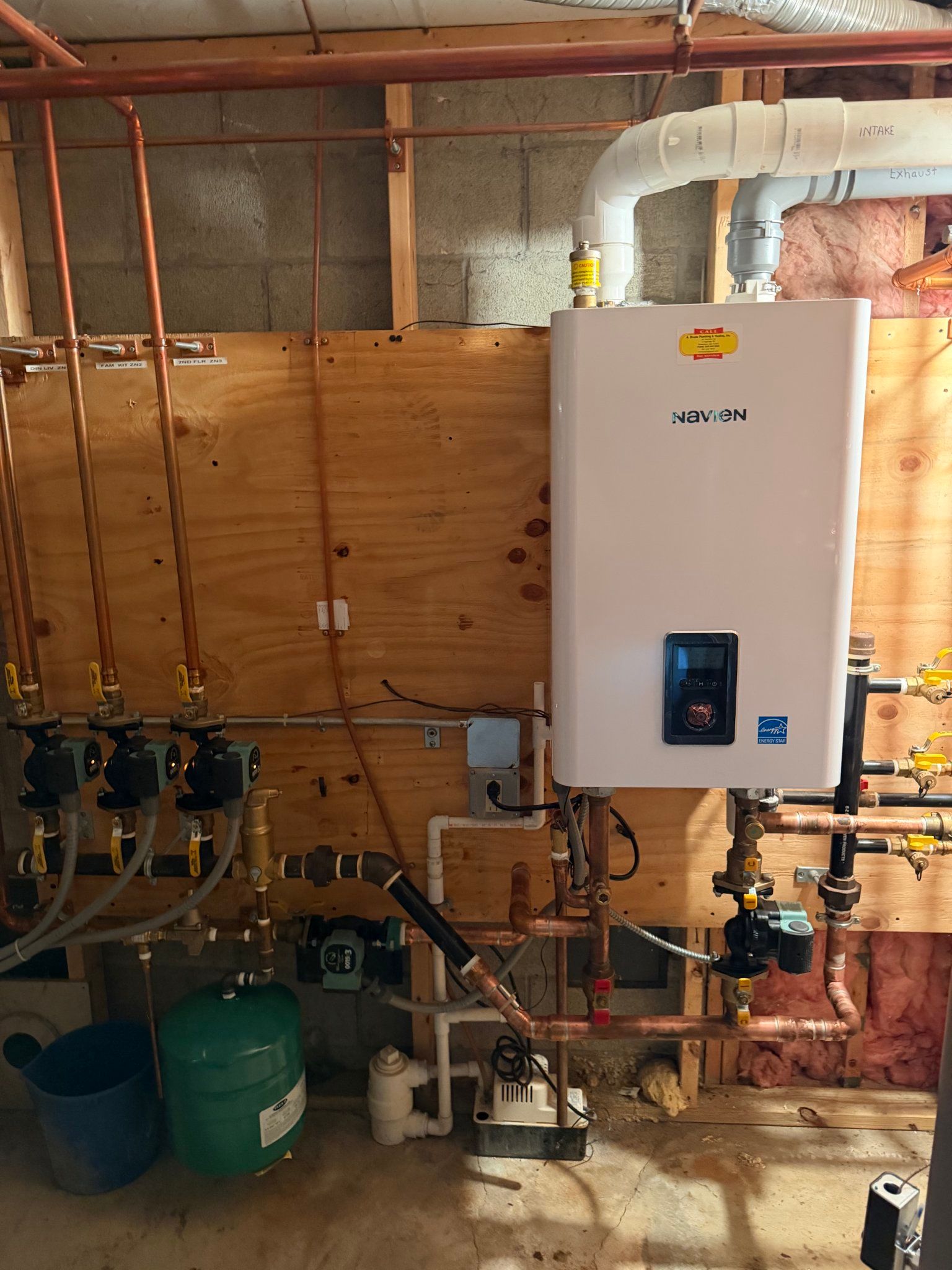 Boiler room with a water heater, exposed pipes, and green tanks on a concrete floor