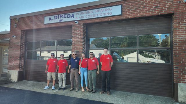 Group of six people in red shirts standing outside a brick storefront with a sign above the entrance