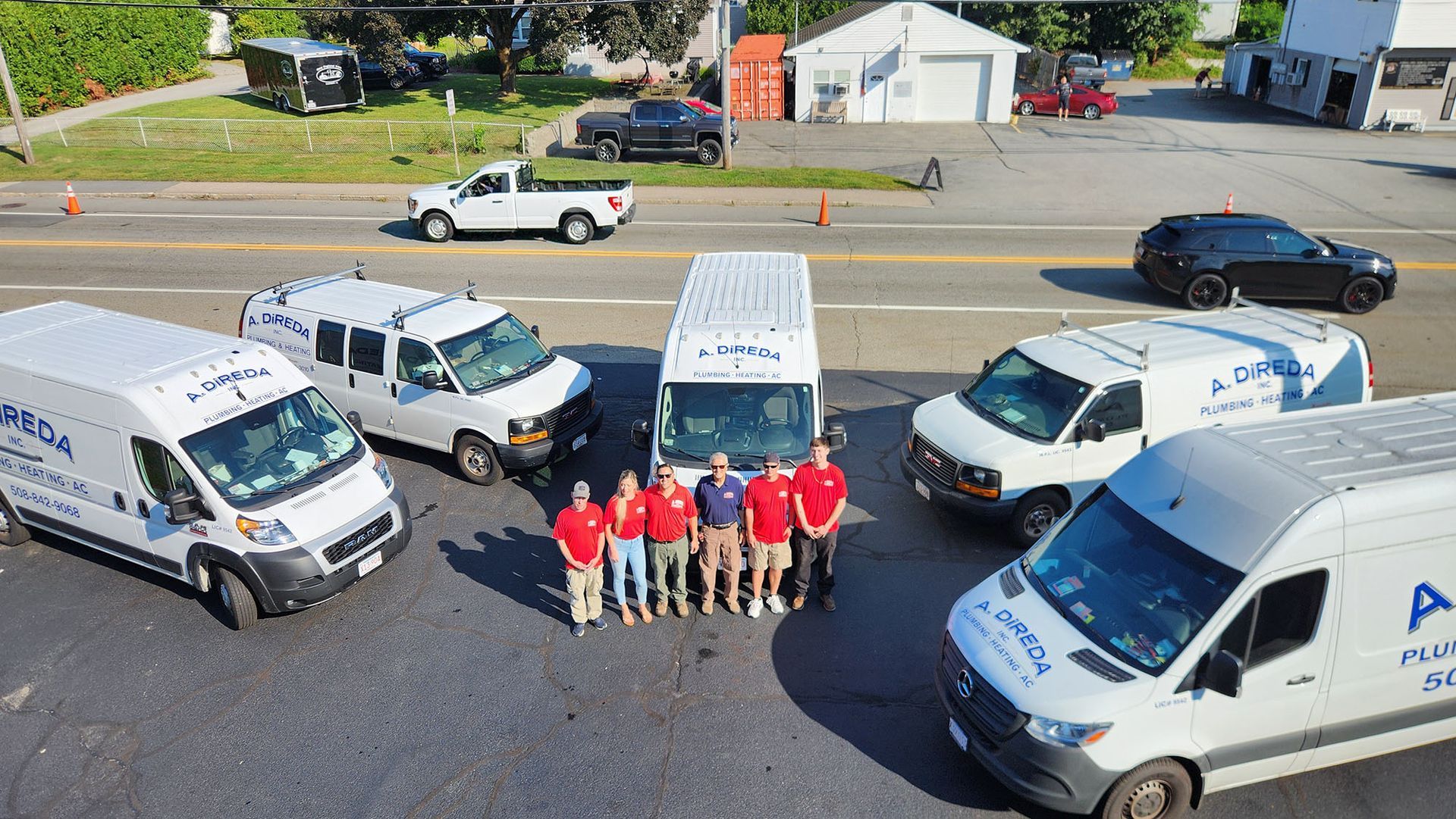 Work trucks and vans parked around a group of workers in red shirts posing outdoors.